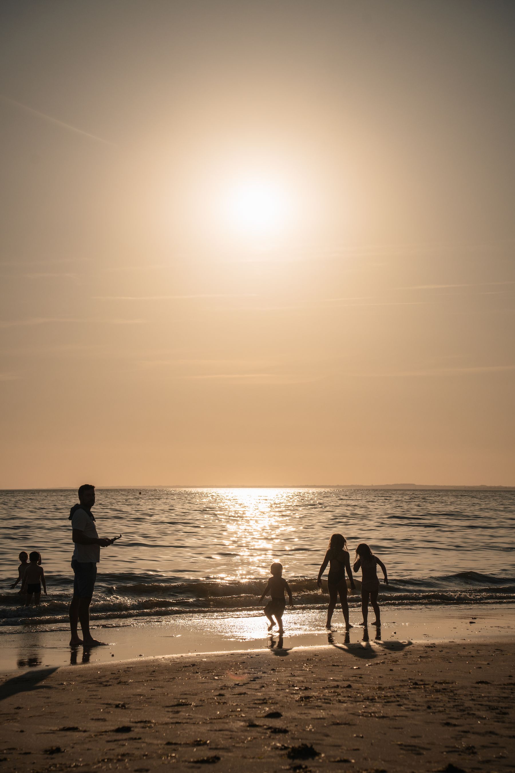 Une famille de dos face au coucher de soleil, les enfants portés à bras.