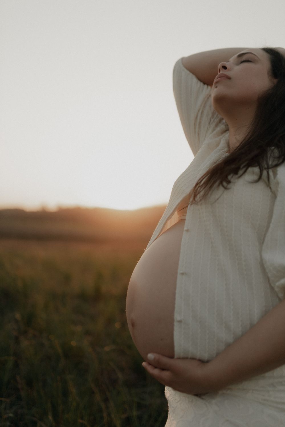 Une femme enceinte, mains posées sur son ventre, dans une lumière dorée.